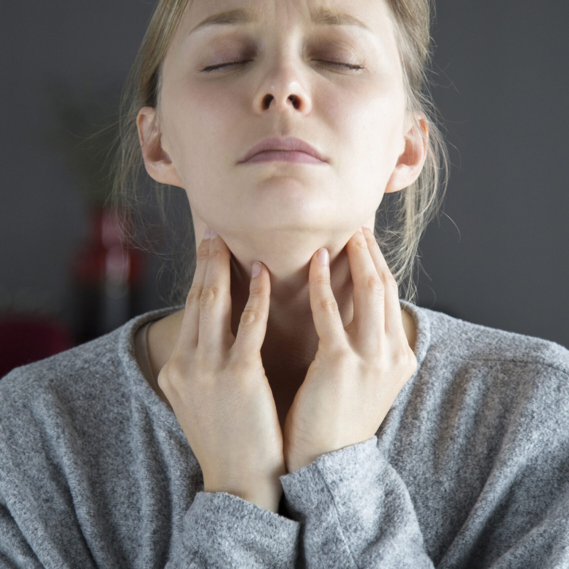 Sick woman with closed eyes having sore throat, touching neck Sick young fair-haired Caucasian woman with closed eyes having sore throat, touching her neck. Illness, pain concept